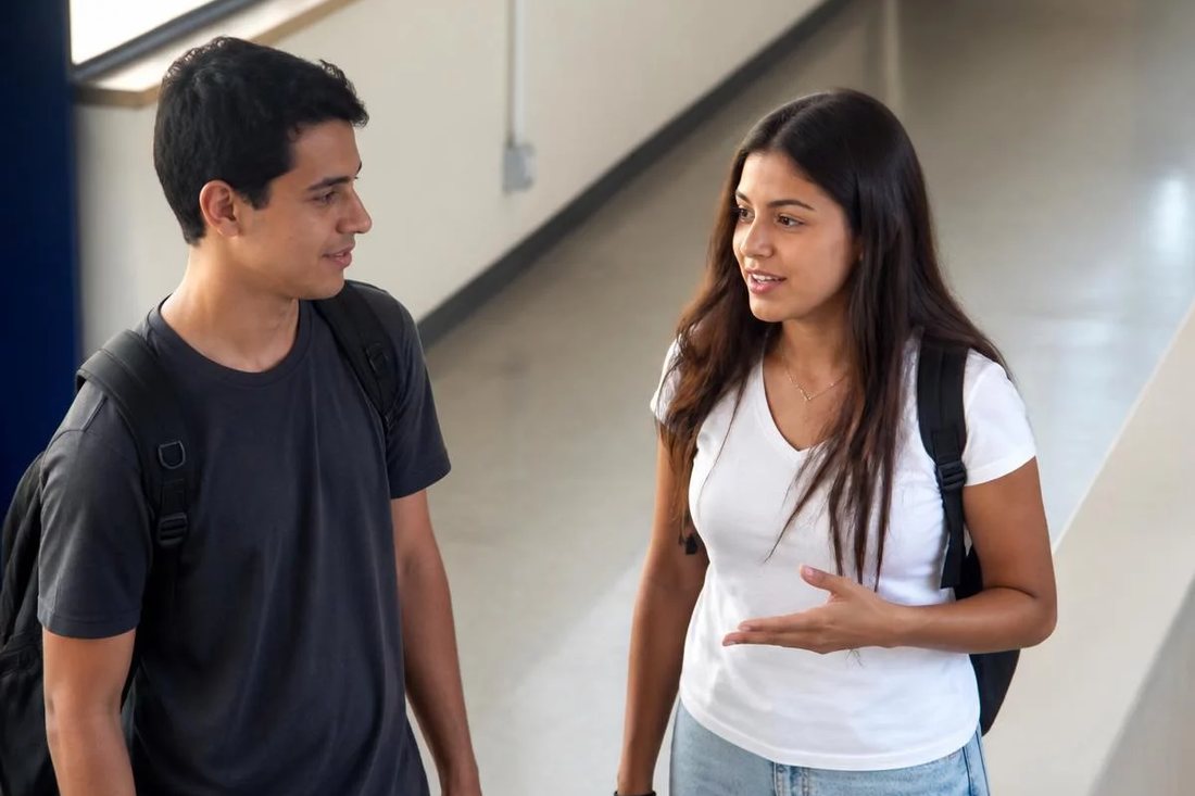 Dois estudantes de mochila continuam a discussão no corredor depois da sessão
